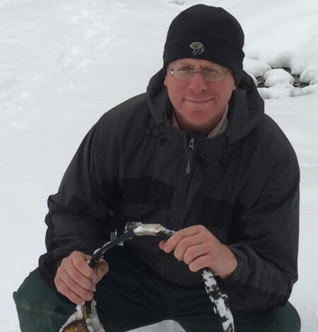 Brent Sigafus kneeling in snow holding a GPS collar.