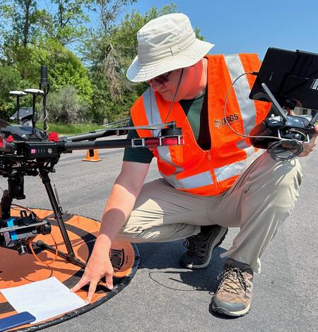Matthew Burgess, kneeling before launchpad, prepares drone aircraft for flight