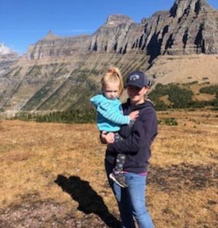 woman wearing baseball cap holding blonde child standing in front of desert background