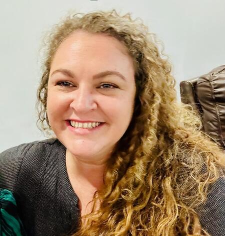 Headshot of a smiling woman with long, light brown curly hair.