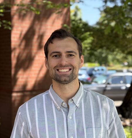 Staff photo of a man with short brown hair smiling in outdoors and wearing a collared shirt. 