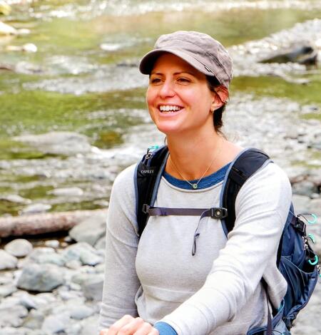 photo of woman smiling and standing near a creek
