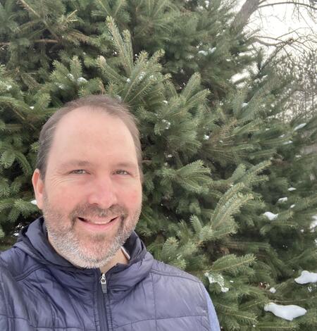 man standing near an evergreen tree wearing a blue jacket