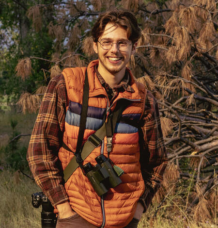photo of matt hixson standing in a field with binoculars and a camera