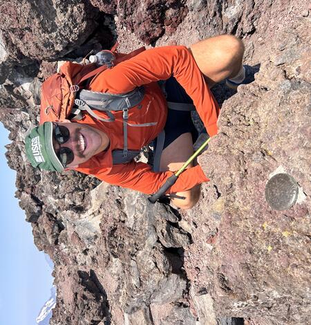 USGS Scientist wearing a USGS logo hat and standing next to a survey monument. 