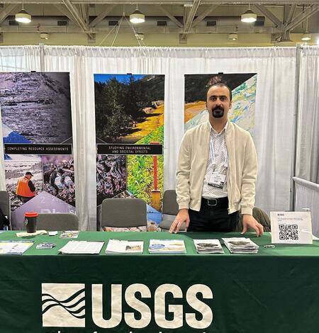 Dr. Iman Salehi Hikouei stands in front of the USGS booth at a conference.