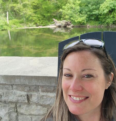 A smiling woman with brown hair standing near and outdoor wall.