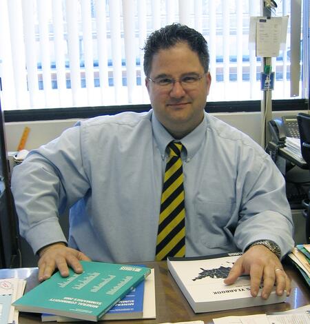 Jason Willett sits at a desk with books on geology on it.