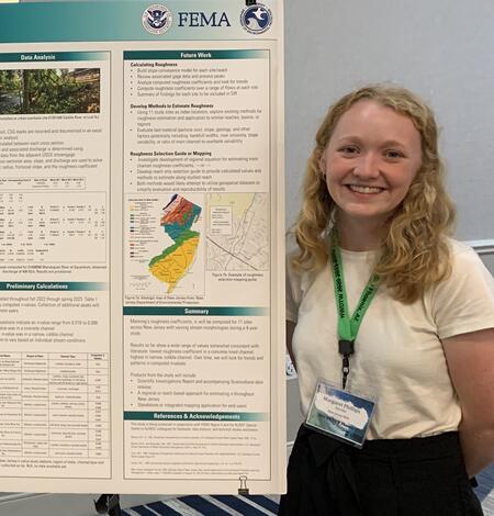 Blonde haired Scientist stands next to a poster of one of her projects.