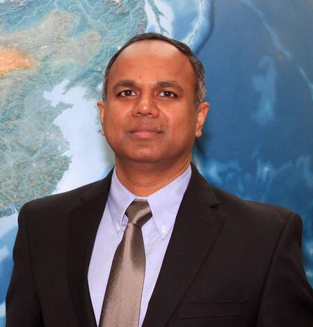 Md Shahriar Pervez staff photo. He is wearing a dark dress coat, a blue button shirt, silver tie and a map as a background.