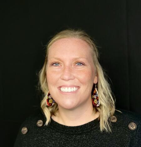 blonde woman smiling wearing a black shirt with a dark background