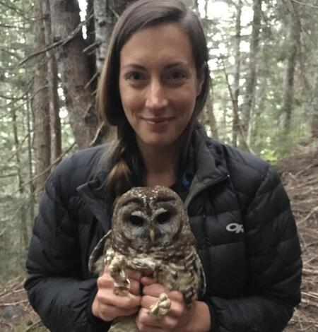 dark haired woman smiling in the forest gently holding an owl