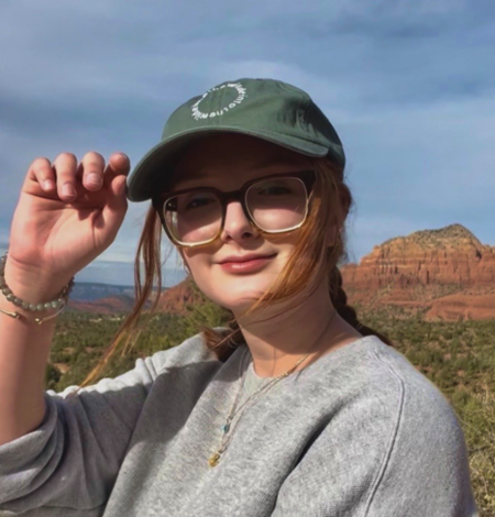 Person wearing glasses and green hat with dryland mountains and valleys