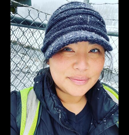 Headshot of a female wearing black snow dusted hat next tp a metal fence on a snowy day