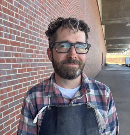 Man with curly hair, glasses, and a flannel shirt. 