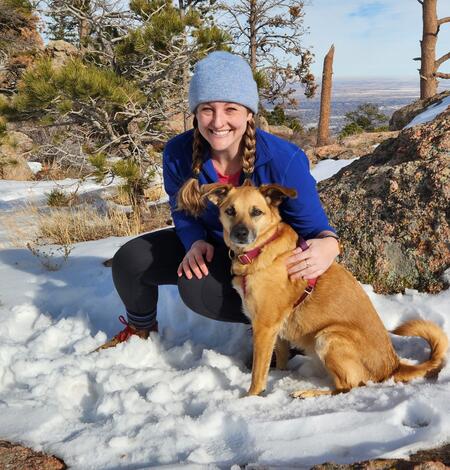 photo of a woman in snow wearing blue hat with dog