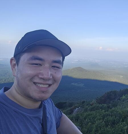 a man with a baseball cap on in front of a large, green valley