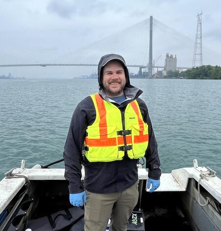 Man standing on boat with large bridge in background
