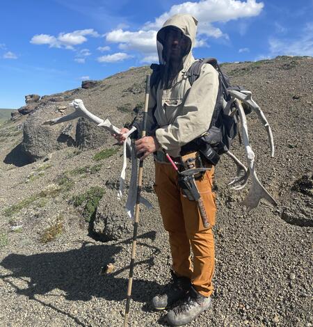 Amit standing on a rocky hill, holding antlers and a measuring stick