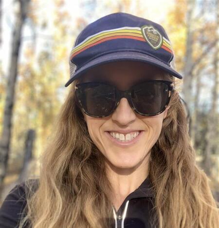 Image of Devyn Orr with a blue hat and sunglass on her face in front of a wooded tree background