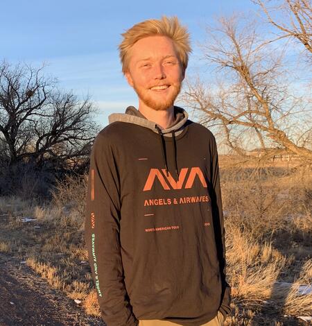 Photo from the waist up of Carter Campbell, standing in front of trees. 