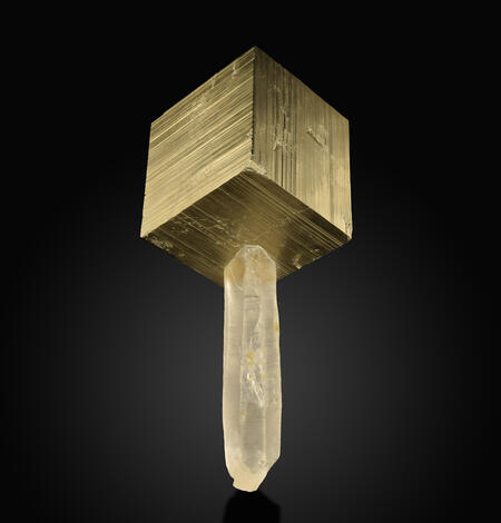 Image shows a cubical sample of pyrite with a quartz crystal extending beneath it