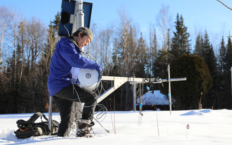 A man kneels down in the snow fixing metal equipment.