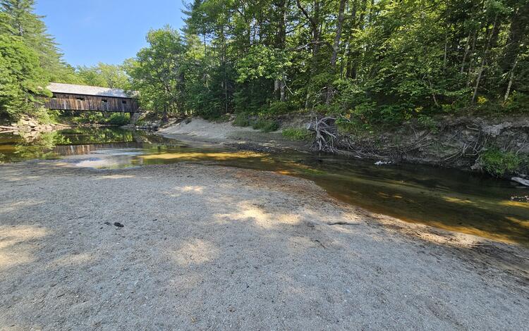A dry riverbed with a covered bridge in the background.