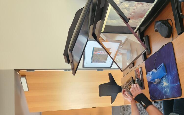 A man in a green shirt with glasses sits at a desk in the Astrogeology Photogrammetry Lab looking at monitor screens.