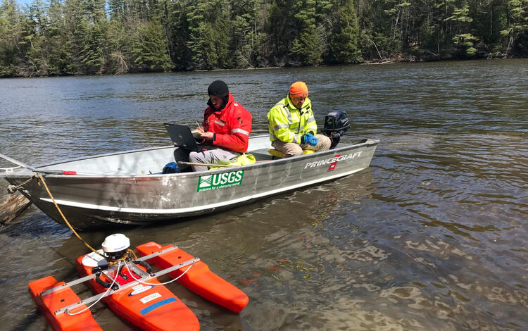 Two USGS employees sit in a motorized boat towing an ADCP