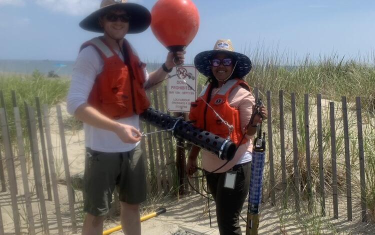 Two scientists in wide brimmed hats and floatation vests holding buoy for deployment 