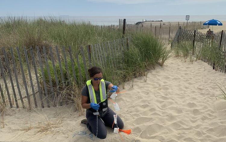 Scientist kneeling on beach next to a water grate prepping a sampler to lower down