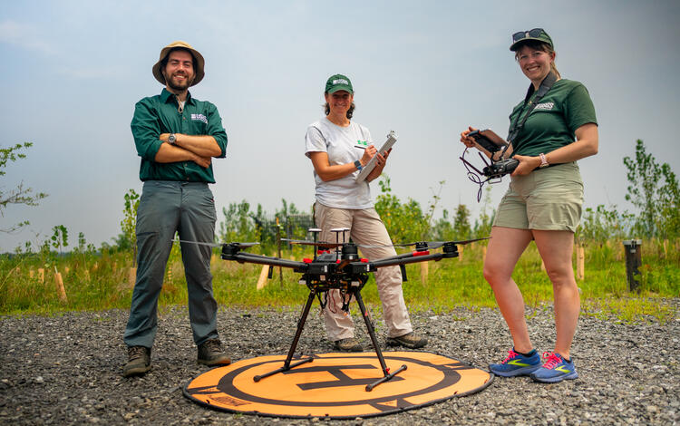 Three people standing behind a drone
