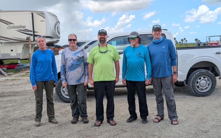 five people stand for a group shot in front of a truck