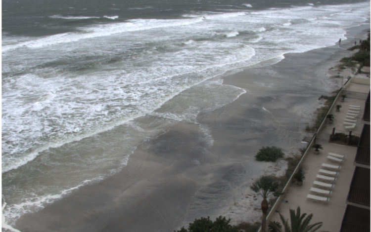 ocean with waves and sandy beach in front long deck with lounge chairs
