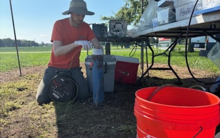 Scientist lowers a tape into a well with buckets and equipment waiting in the foreground