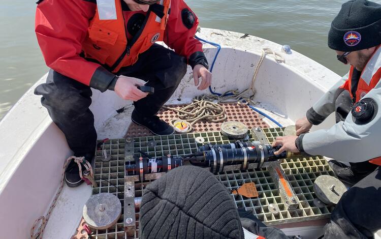 Three people on a small boat working with a small piece of equipment