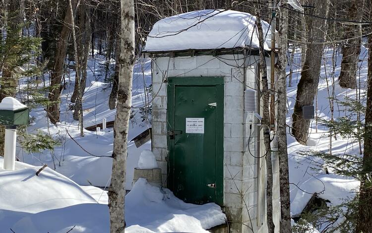 A streamgage house in a snowy, forested landscape.
