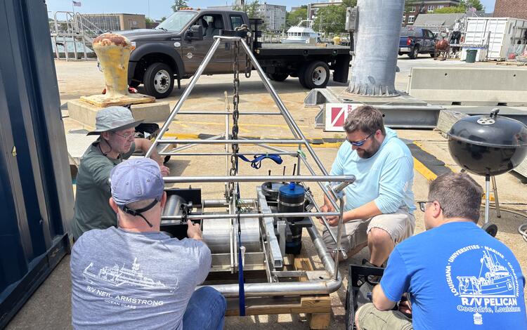 four people around a large piece of equipment outside by the water