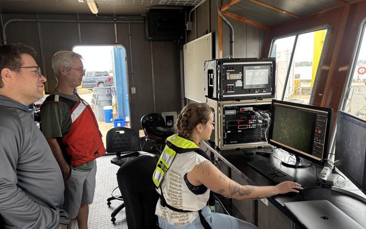 Three people staring at computer screens showing images of the seafloor