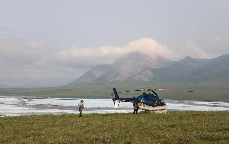 two people near helicopter with mountains in the background