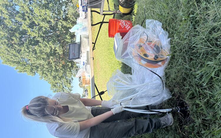 USGS scientist lowers hoses from a pump wrapped in protective plastic down into a well