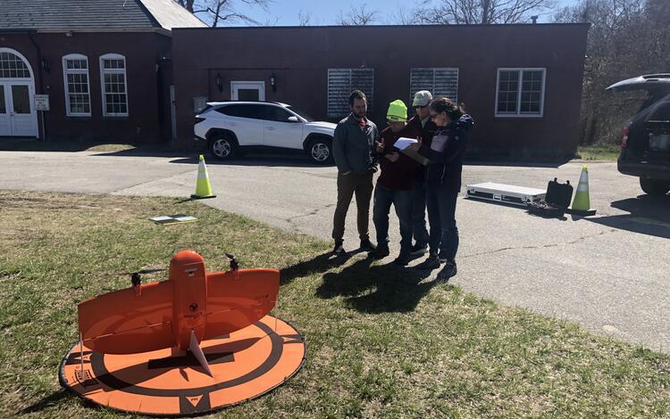 four people standing together looking at screen outside with drone on the ground