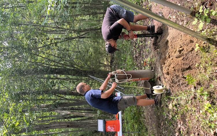 Two men install a groundwater well in the woods.