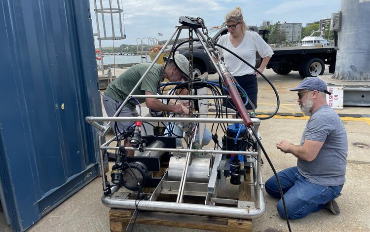 Three people working on a big instrument on a dock