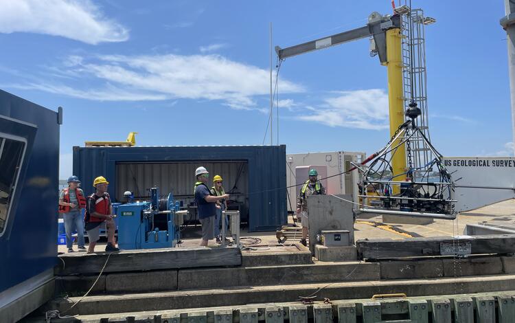 People on dock lowering large piece of equipment into the water