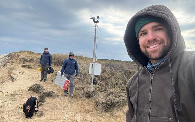 Three people on beach with camera mounted on tall pole