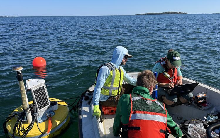 Three people sit in a boat surrounded by water and a buoy.