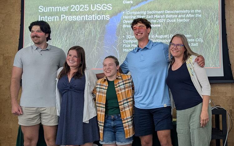 four people posing for photo together in front of PowerPoint presentation