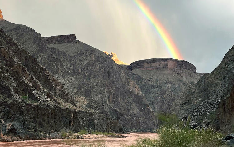 A rainbow in a stormy sky arches over Grand Canyon and the Colorado River
